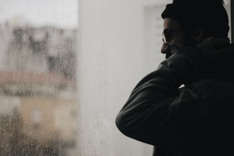 Man looking at rain outside of window