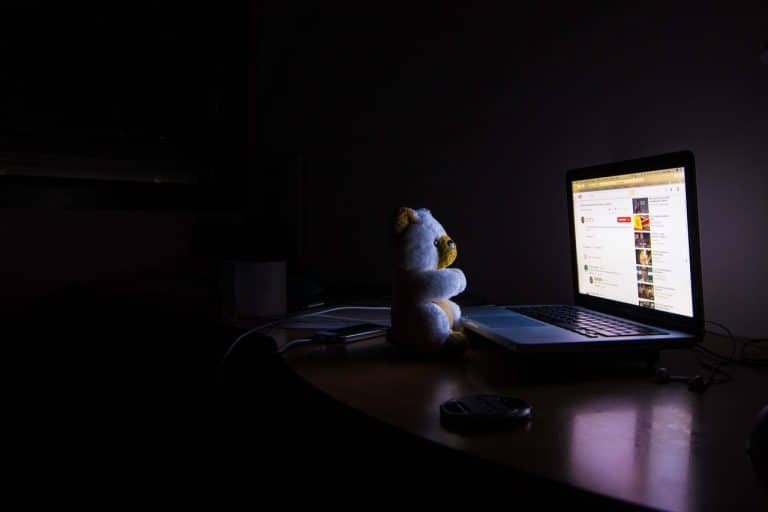 Teddy bear in darkened room facing computer screen