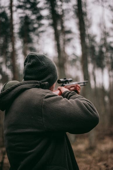 Behind shot of a man with a hunting rifle in the woods.