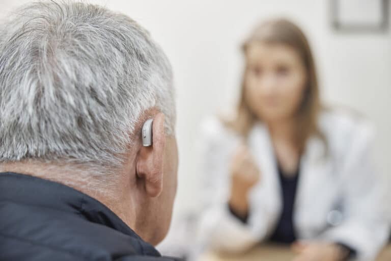 Anterior view of a man wearing hearing aids, talking to an audiologist