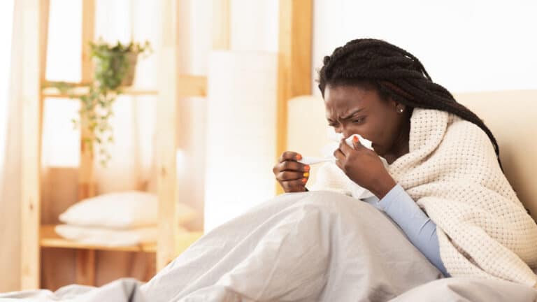 Woman with a sinus infection sneezing into a tissue in bed.