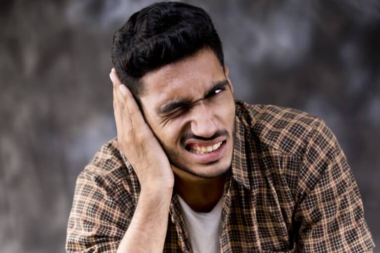 Man with ear pain holding his right ear.